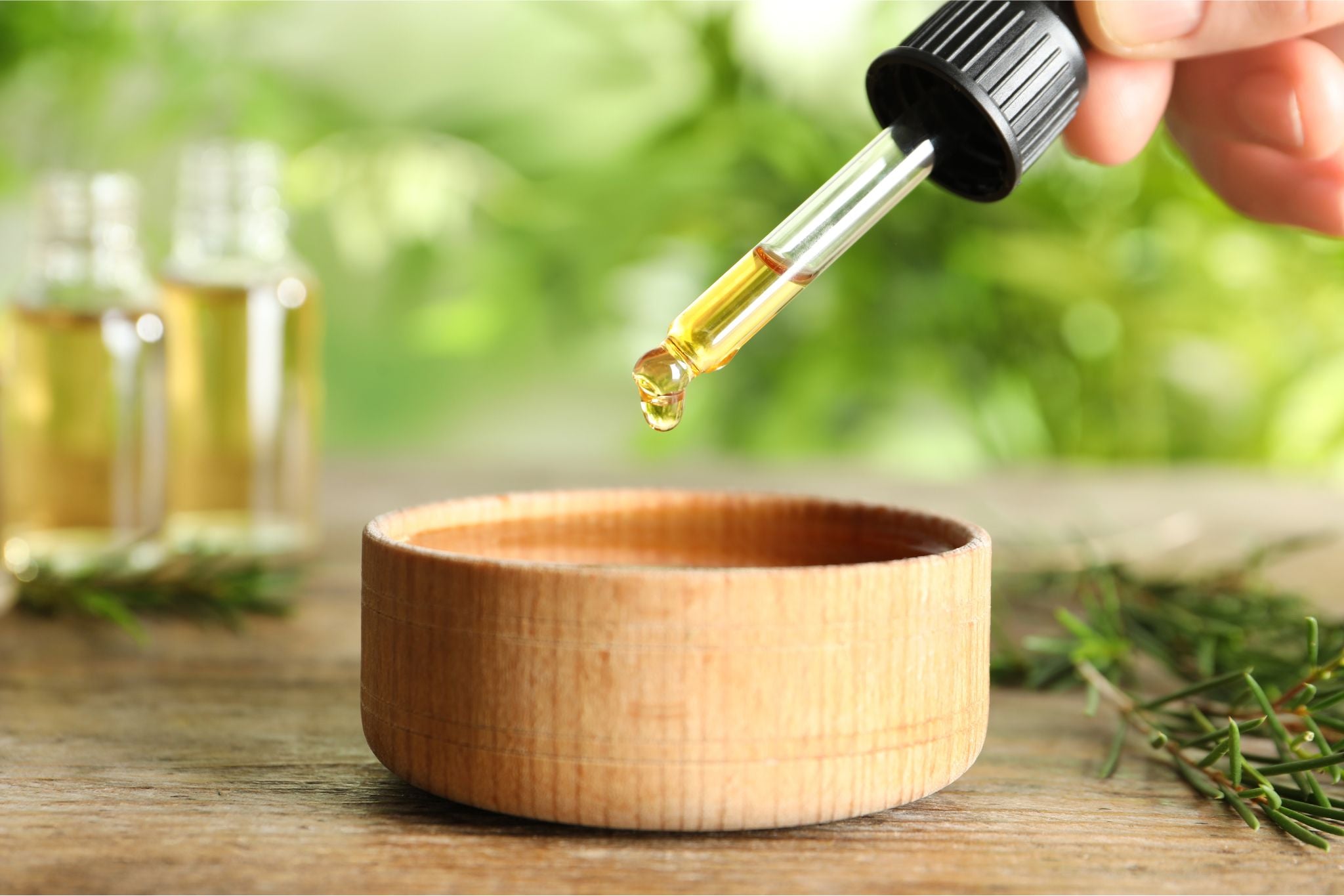 Pipette mit gelbem Öl über einer kleinen Holzschale, im Hintergrund Glasfläschchen und Rosmarinzweige