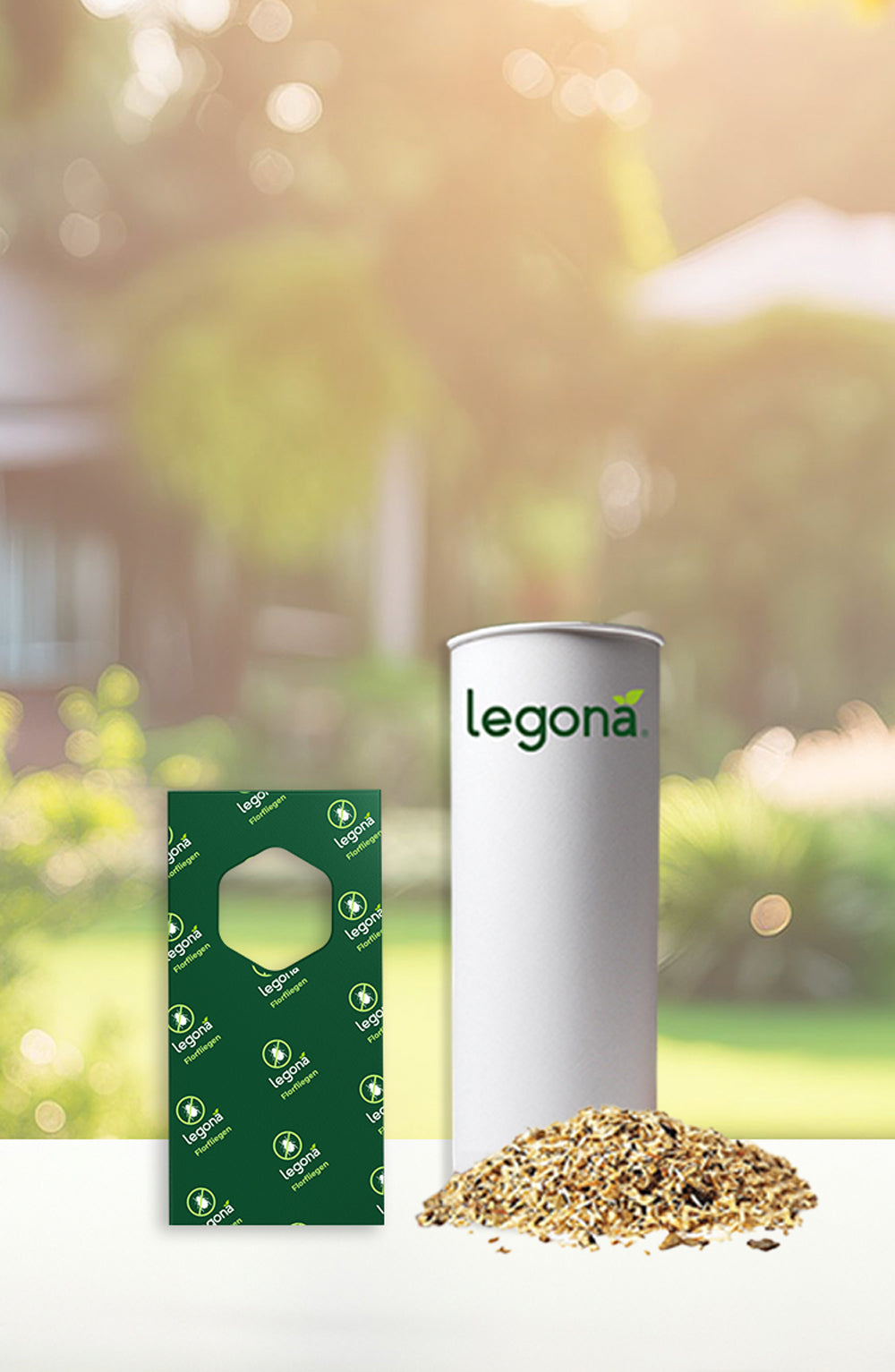 Zylindrische weiße Verpackung mit grünem Schriftzug "legona" neben grünem Trägerstreifen und einem Haufen Granulat auf weißer Oberfläche vor unscharfem Garten-Hintergrund
