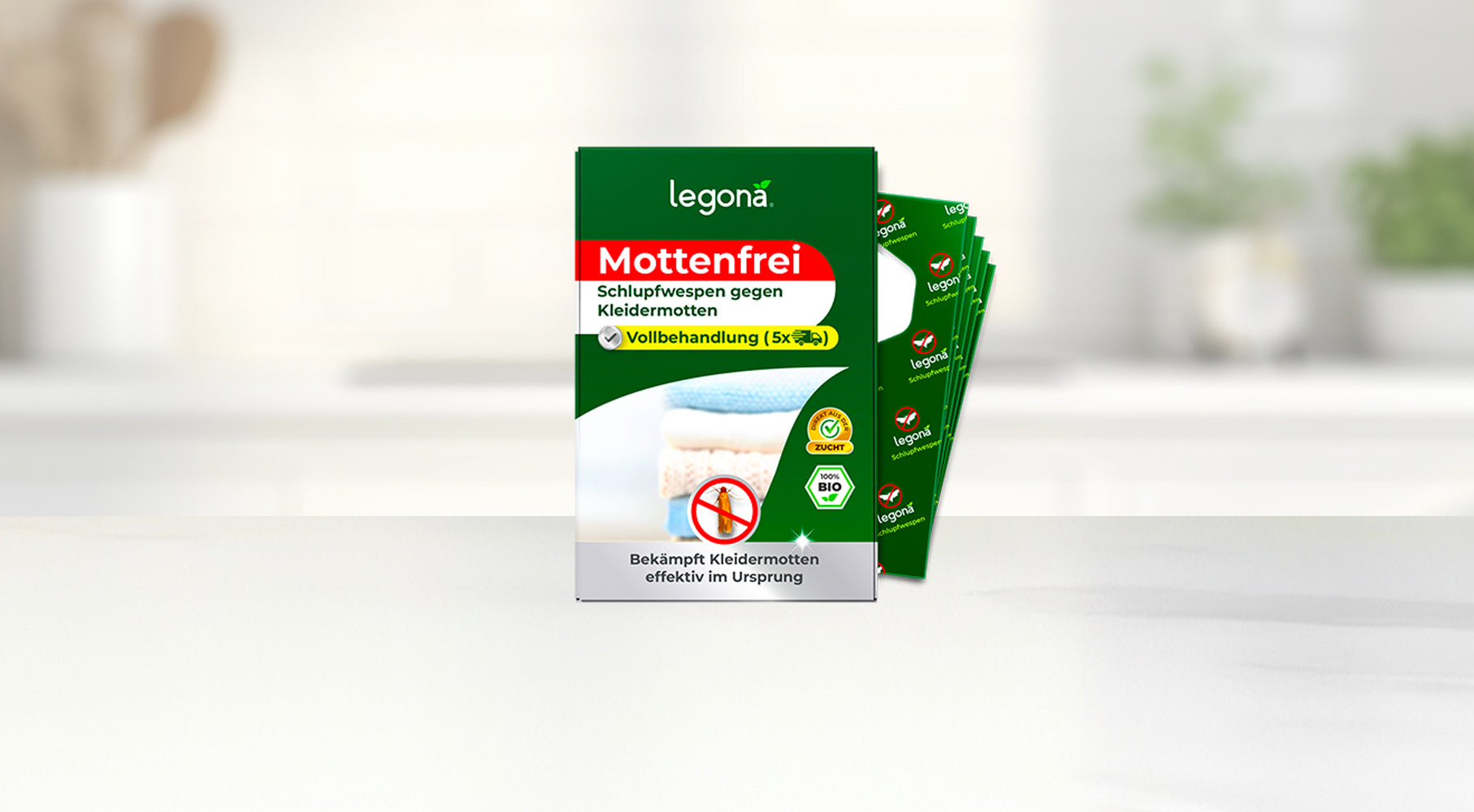 Verpackung von Legona Mottenfrei mit Text zu Schlupfwespen gegen Kleidermotten, daneben mehrere grüne Trägerstreifen im Fächer vor unscharfem Küchenhintergrund