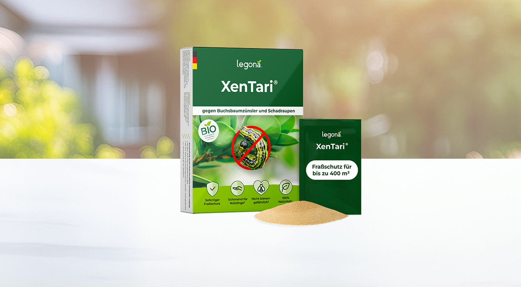 Verpackung von Legona XenTari mit Bild einer Raupe auf einem Blatt, durchgestrichen mit rotem Kreis, daneben ein grünes Pulverhäufchen und ein einzelnes Pulverpäckchen mit der Aufschrift 'Fraßschutz für bis zu 400 m²' vor unscharfem Garten-Hintergrund